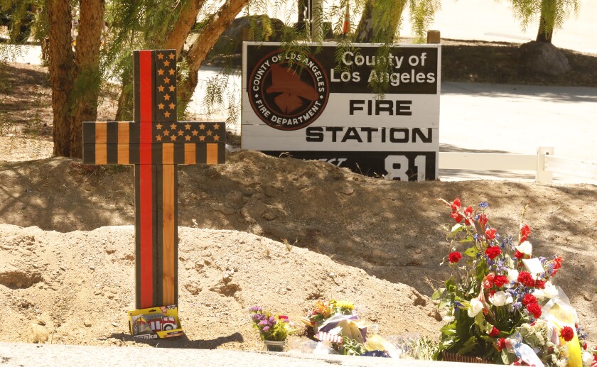 A wooden cross and flowers outside a fire station