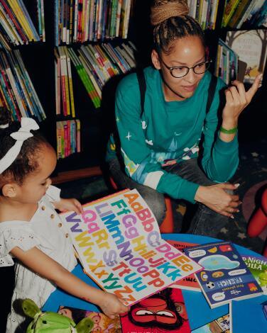 A woman and a little girl look at books at a low table, with bookshelves behind them