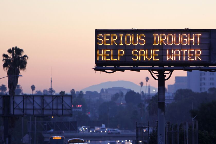 A view of a Los Angeles freeway at dusk, capped by an illuminated sign that reads: SERIOUS DROUGHT. HELP SAVE WATER.