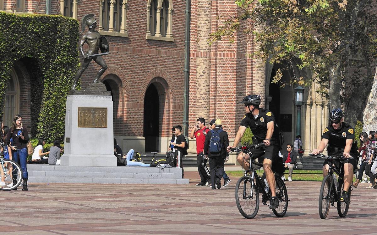 Campus police officers ride bikes through a central plaza at USC as students gather around the Tommy Trojan statue