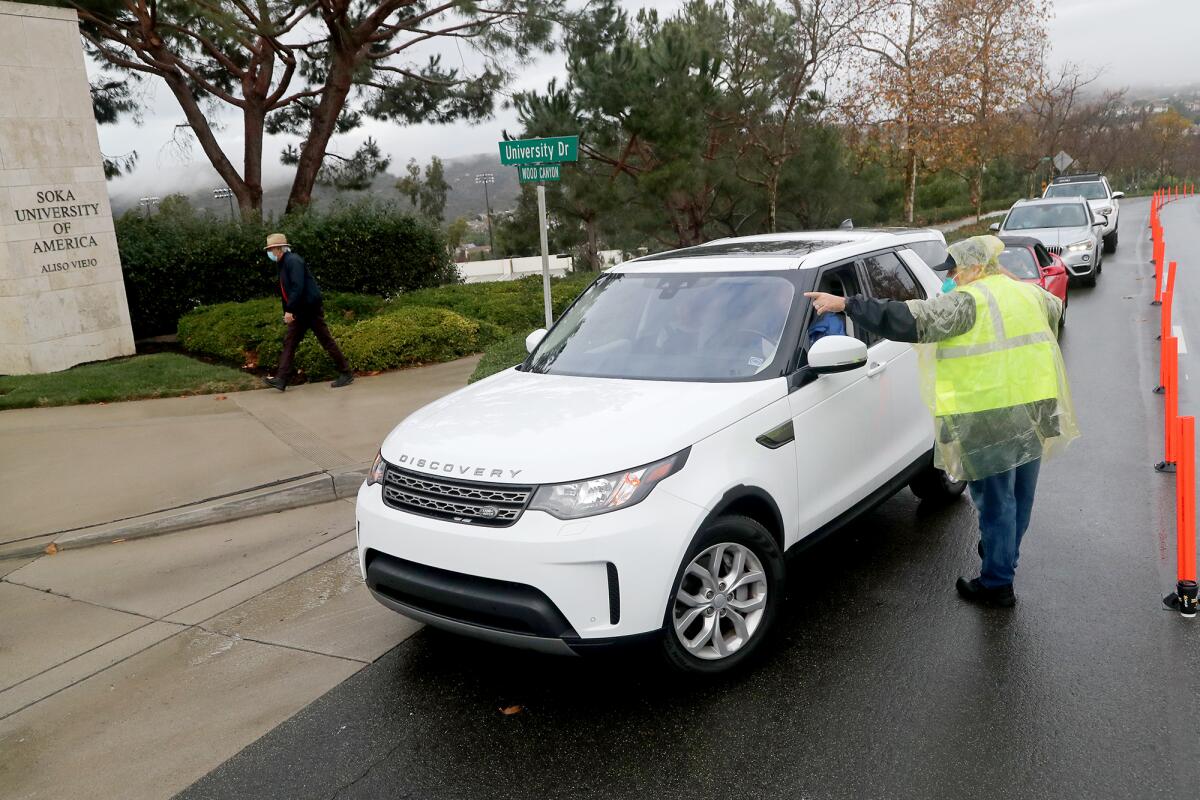 An Orange County COVID-19 response team member directs drivers to the gymnasium at Soka University.