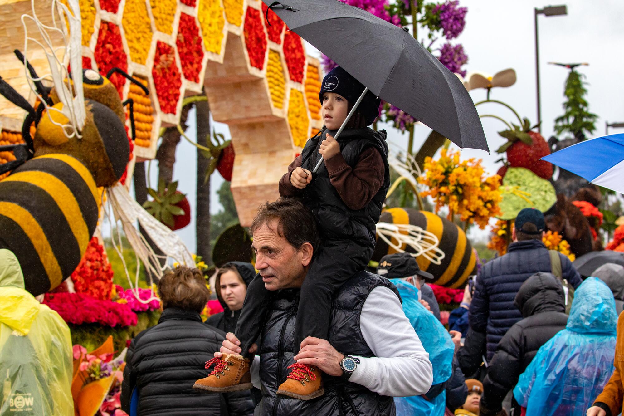 Dad with a son on his shoulders holding an umbrella in a crowd