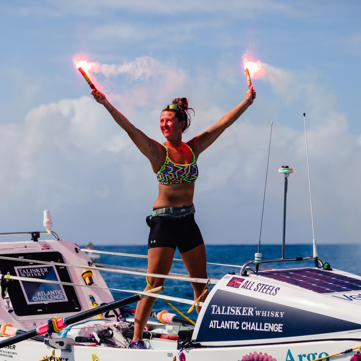 A woman standing in a rowing boat celebrates with her hands in the air