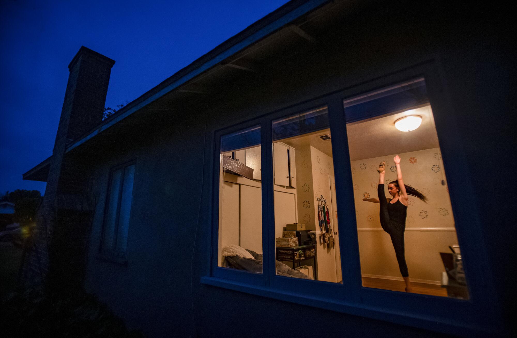 A girl dances alone in a lighted home as night falls