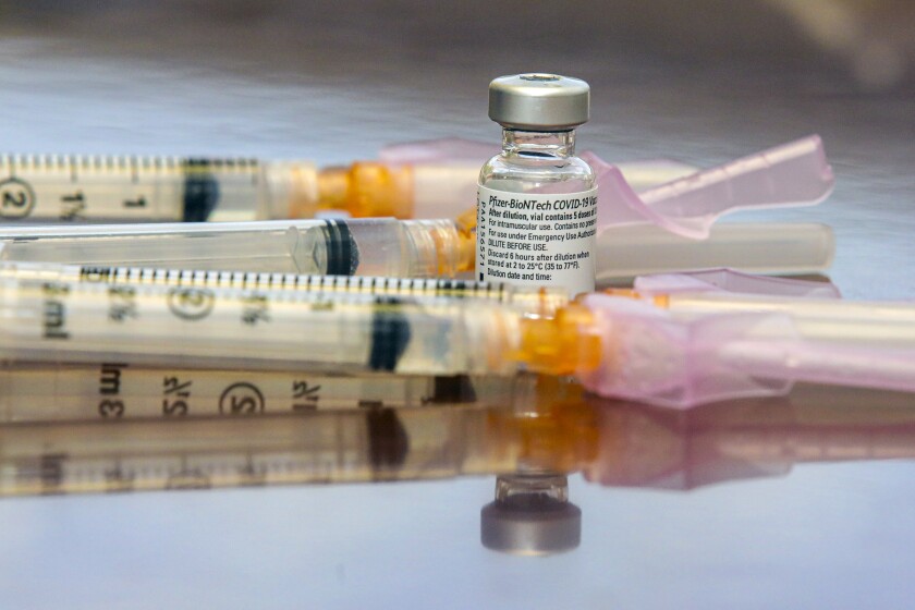 Syringes sit next to a vial of vaccine.
