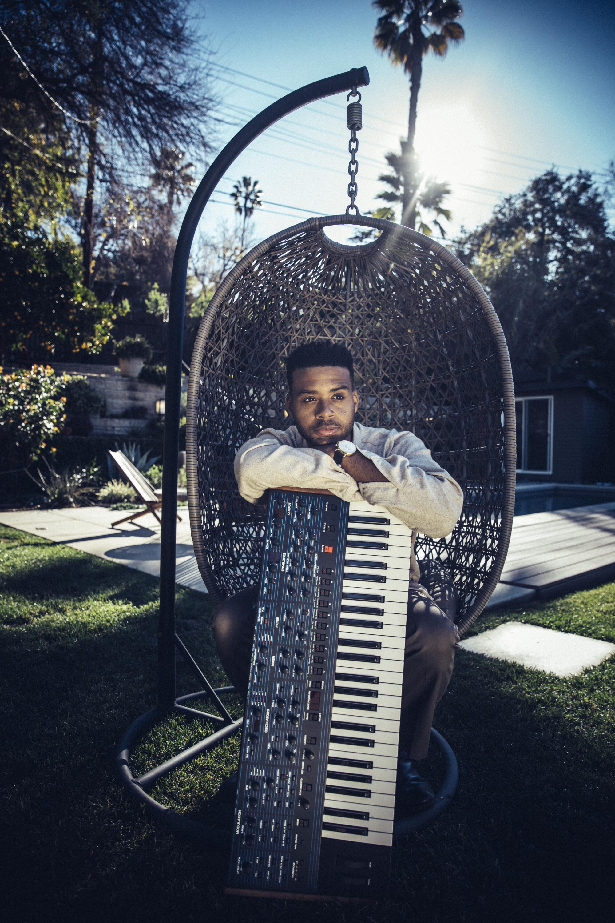 A man in a basket chair outside leaning on a keyboard