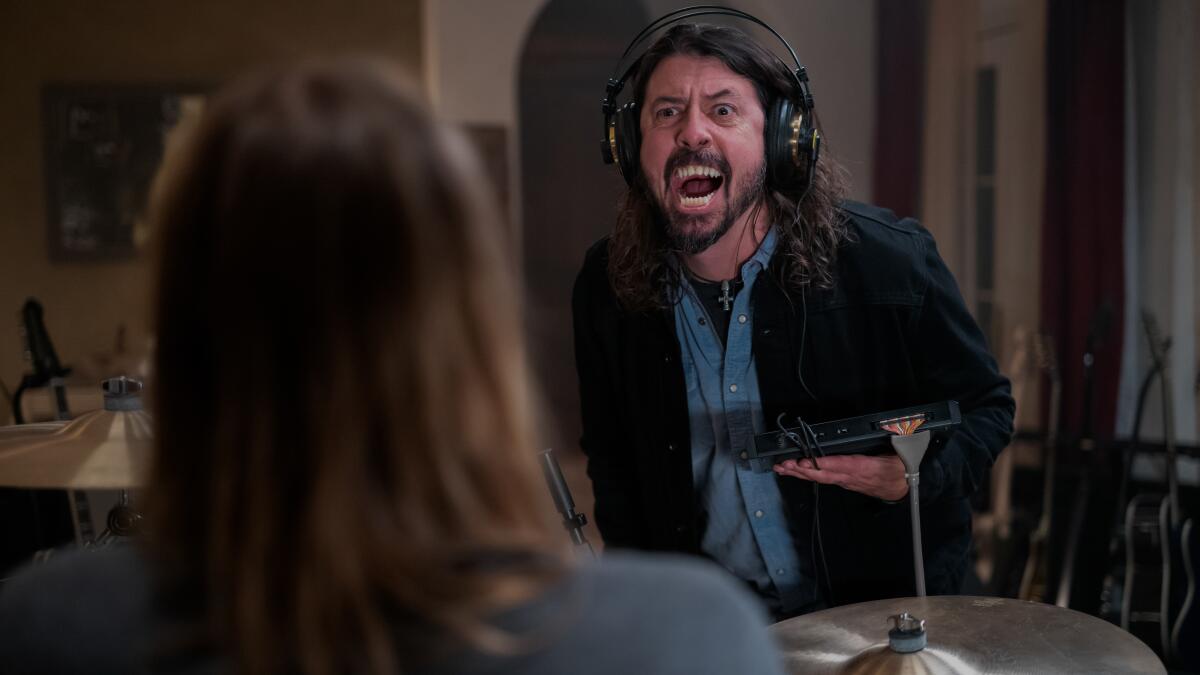 A man standing while wearing headphones yells at another person.