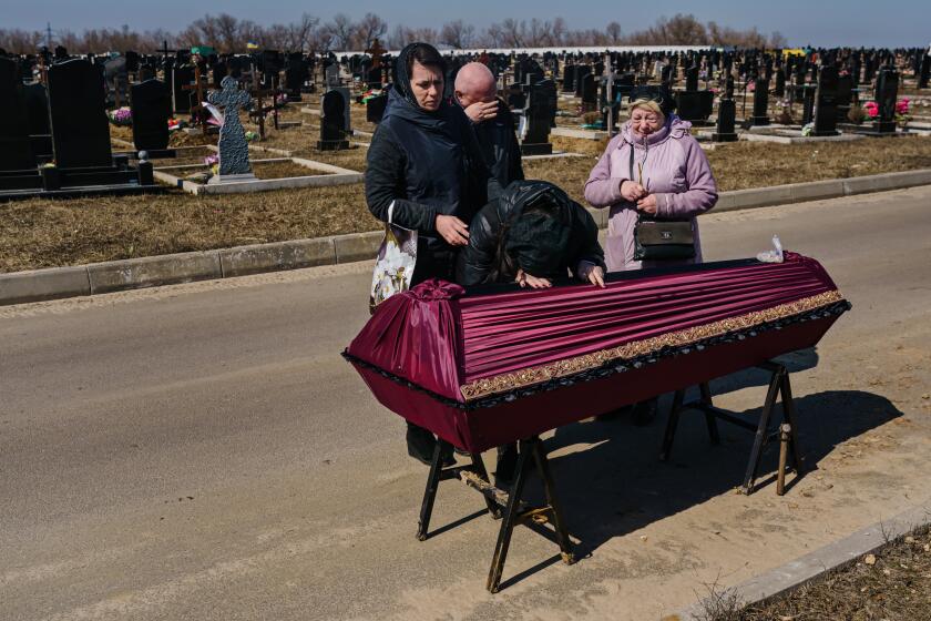 KHARKIV, UKRAINE -- MARCH 24, 2022: Julia Romantschenko, 34, granddaughter, lowers her head to bid farewell to her grandfather, as Igor Romantschenko, 60, son, center, an unnamed family friend, left, and Liubov Romantschenko, 62, daughter-in-law, right, attend the funeral for Boris Romantschenko, in Kharkiv, Ukraine, Thursday, March 24, 2022. Romantschenko survived HitlerOs wrath over Europe, survived forced labor and detention in four concentration camps during World War II. He was killed by Russian bombardment struck his apartment building in Kharkiv. (MARCUS YAM / LOS ANGELES TIMES)