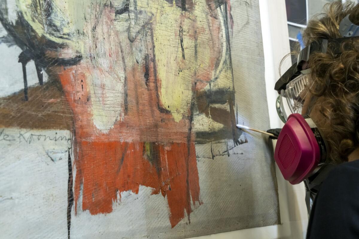 A woman works to remove layers of varnish from a painting.