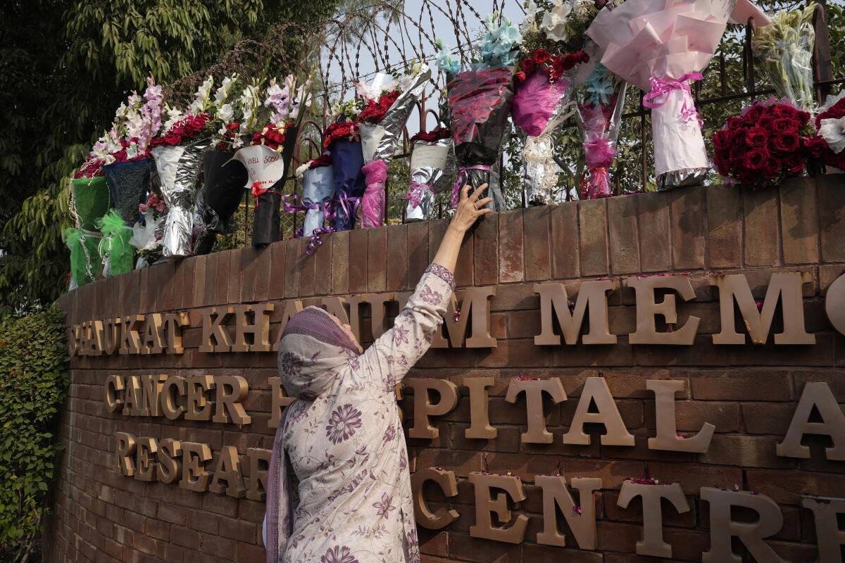 Woman reaching up to place a bouquet on top of a hospital wall
