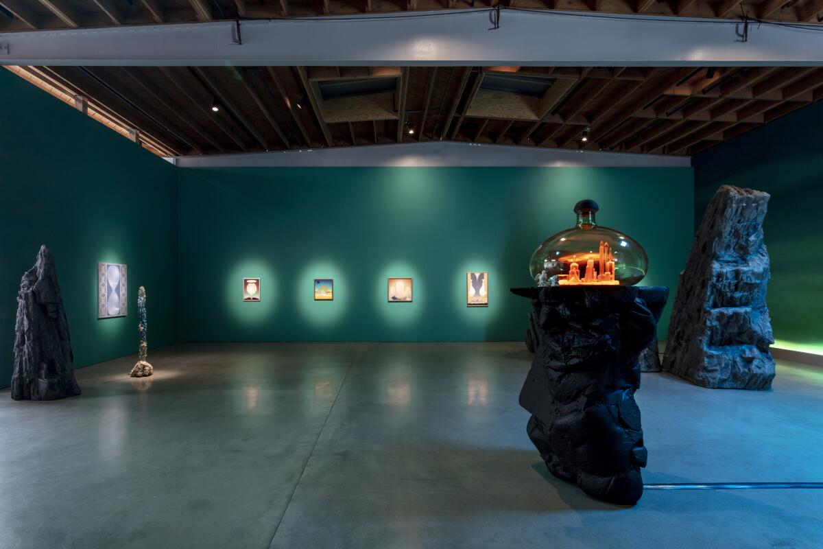 A dimly lighted gallery shows a glass dome with an illuminated model of a city displayed on a rock plinth.