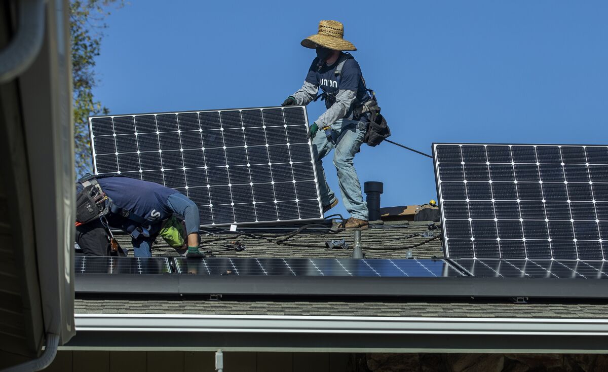Two workers install solar panels on a roof.
