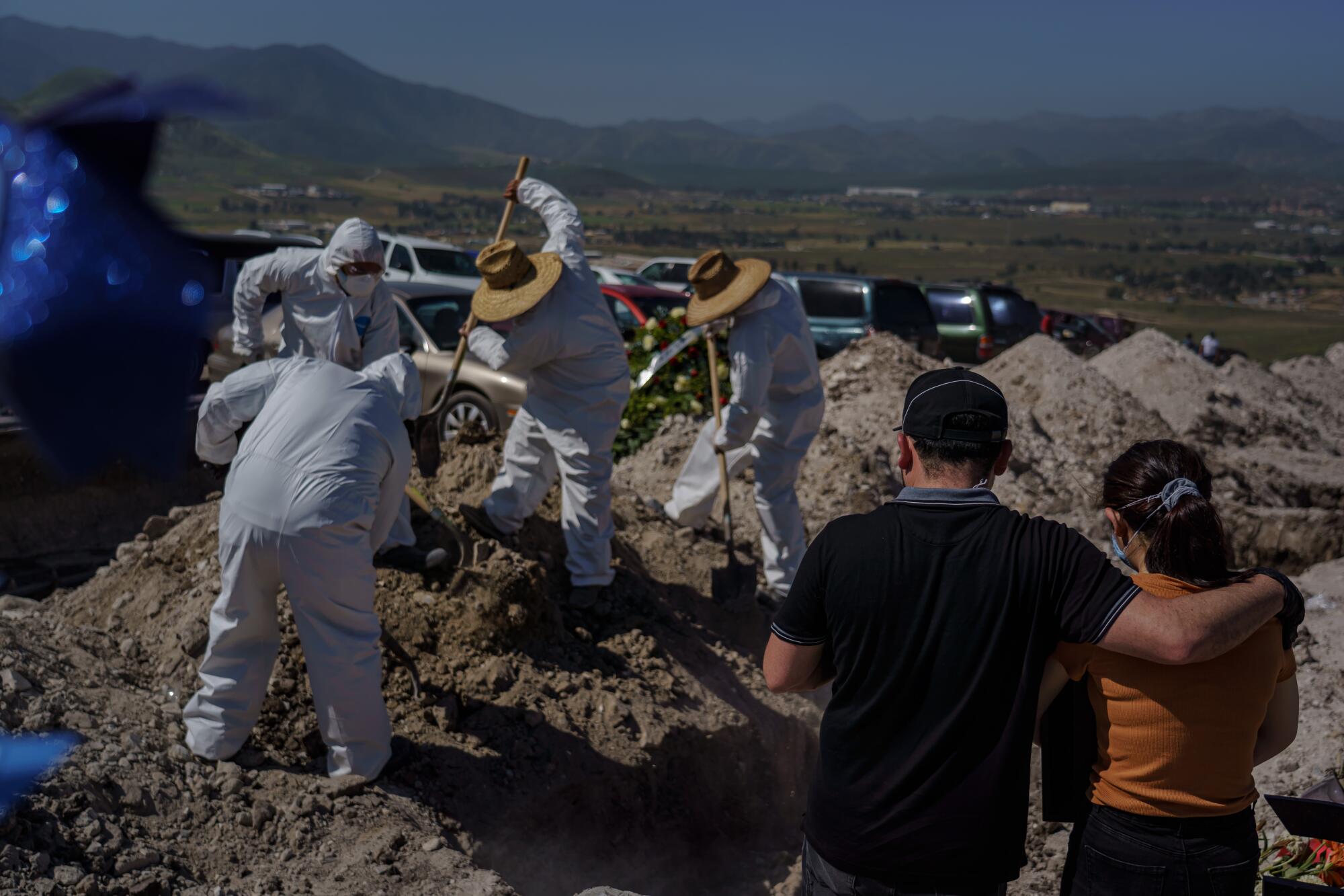 Family members watch from a distance as workers in protective suits bury a relative at Tijuana's Municipal Cemetery No. 13.