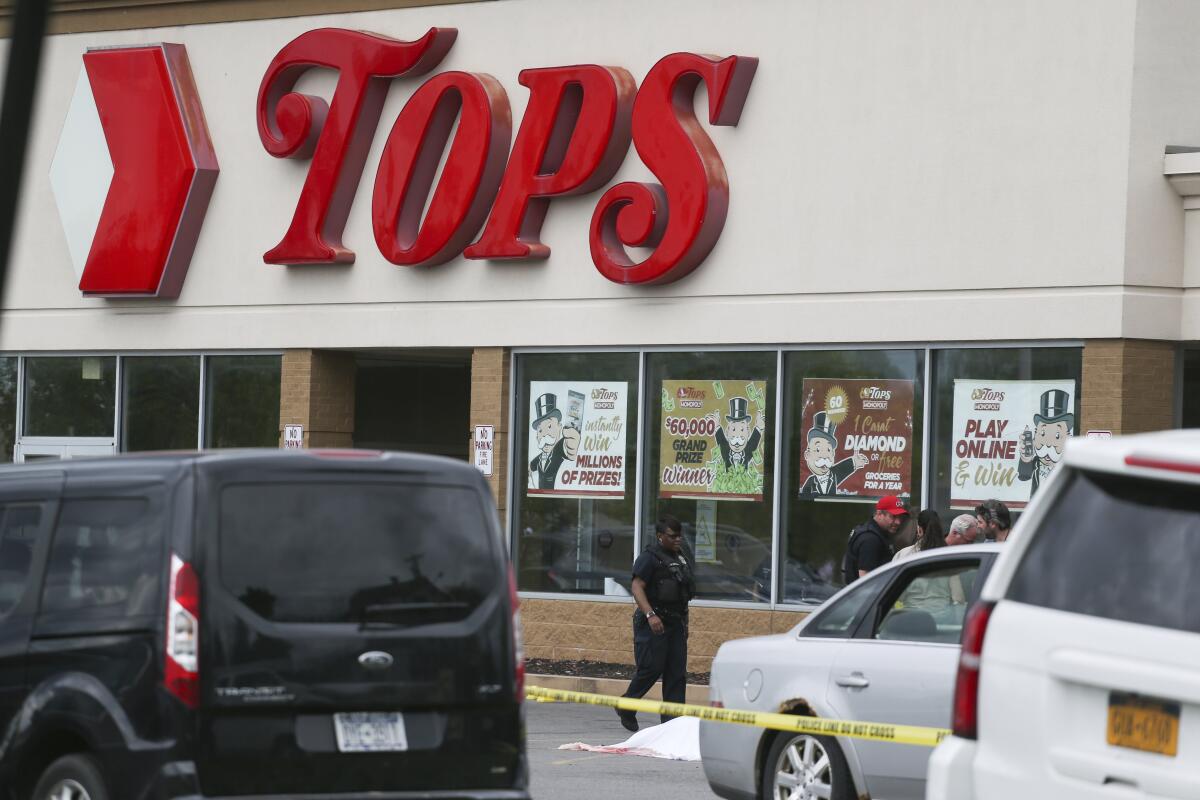 Crime scene tape stretches between parked cars in front of a Tops Friendly Markets store.