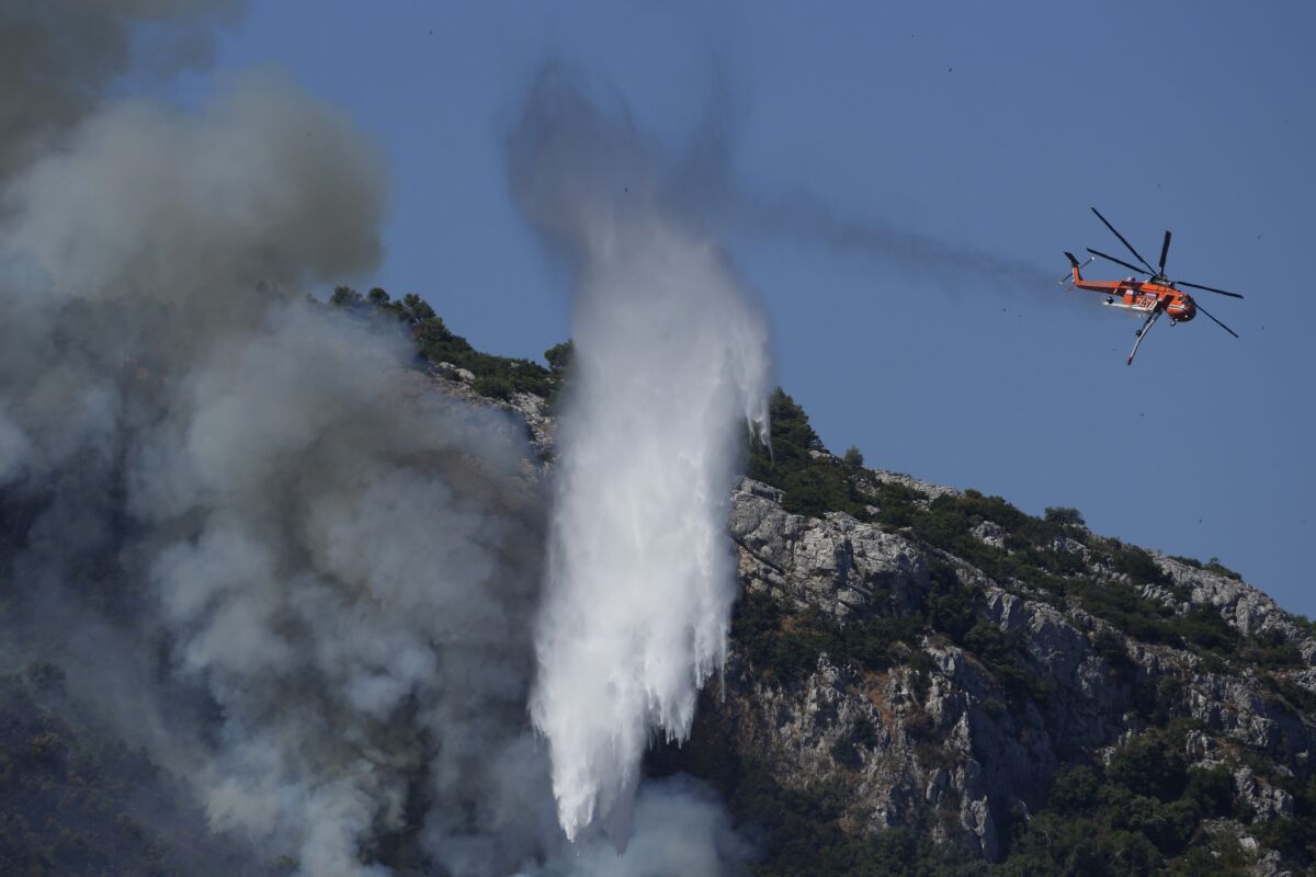 A helicopter drops water on a fire during a wildfire near Malakasa, in northern Athens, Greece, Saturday, Aug. 7, 2021. Wildfires rampaged through massive swathes of Greece's last remaining forests for yet another day Saturday, encroaching on inhabited areas and burning scores of homes, businesses and farmland. (AP Photo/Petros Karadjias)