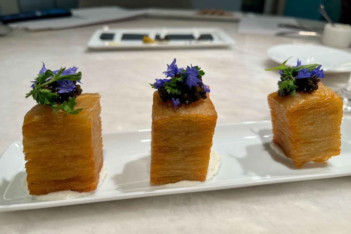 Three tall potato rectangles garnished with caviar on top, sitting on a white rectangular plate