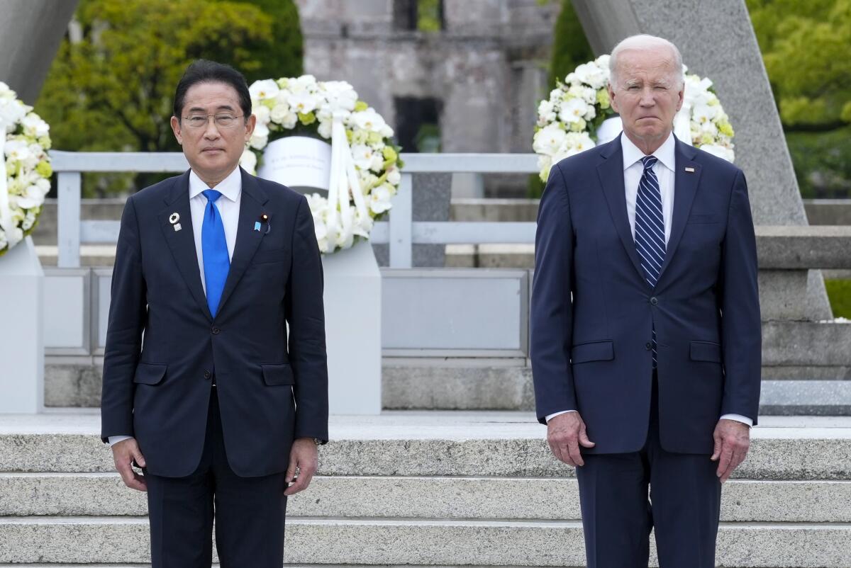 Japanese Prime Minister Fumio Kishida and President Biden standing in front of a monument decorated with white floral wreaths