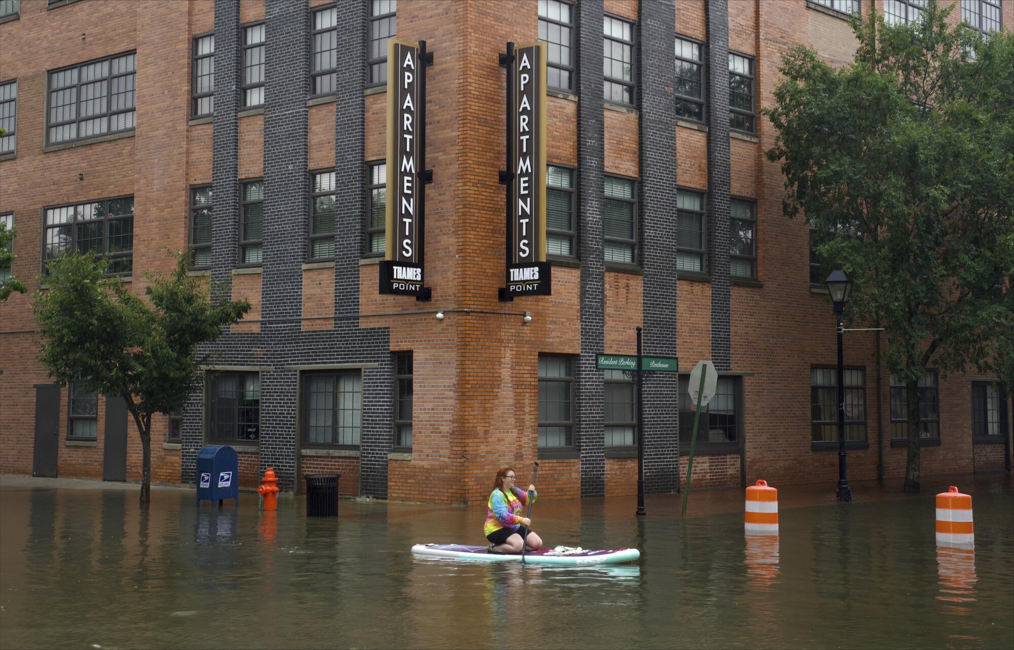 A woman paddles a boat down a flooded city street.