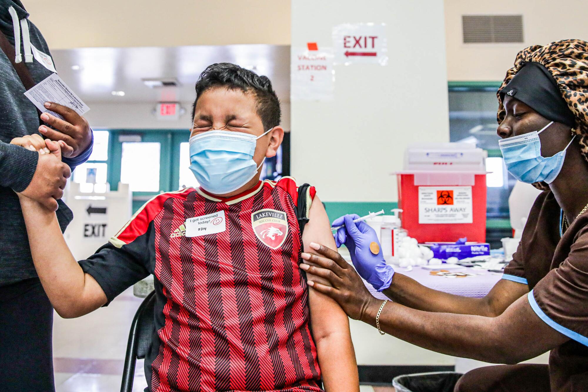 A boy squeezes his eyes shut and grips his mother's hand as he gets a shot.