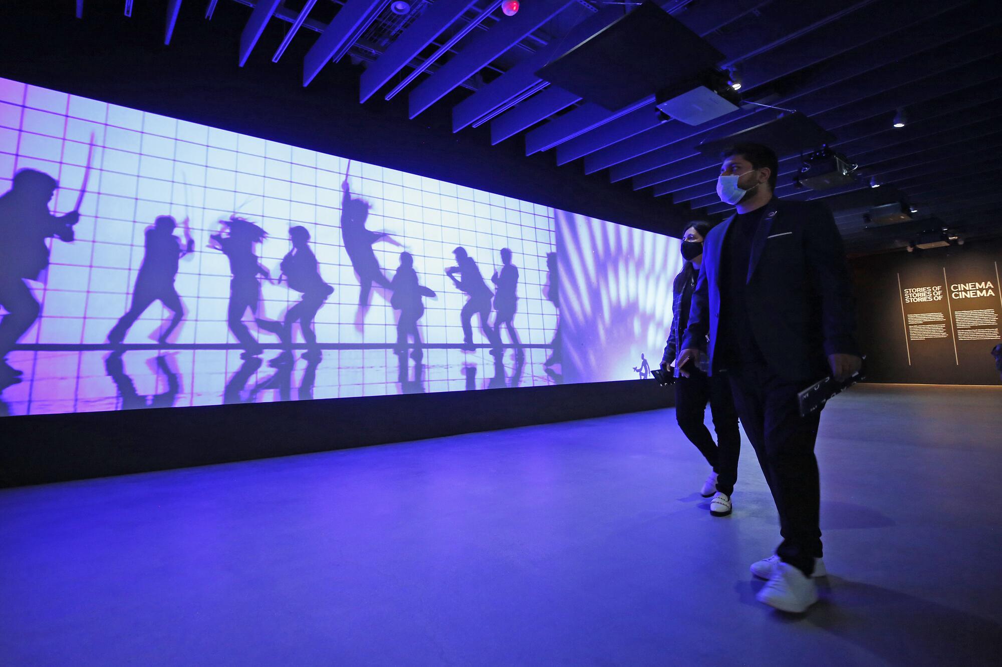 People look at an illuminated wall with images of people dancing and leaping.