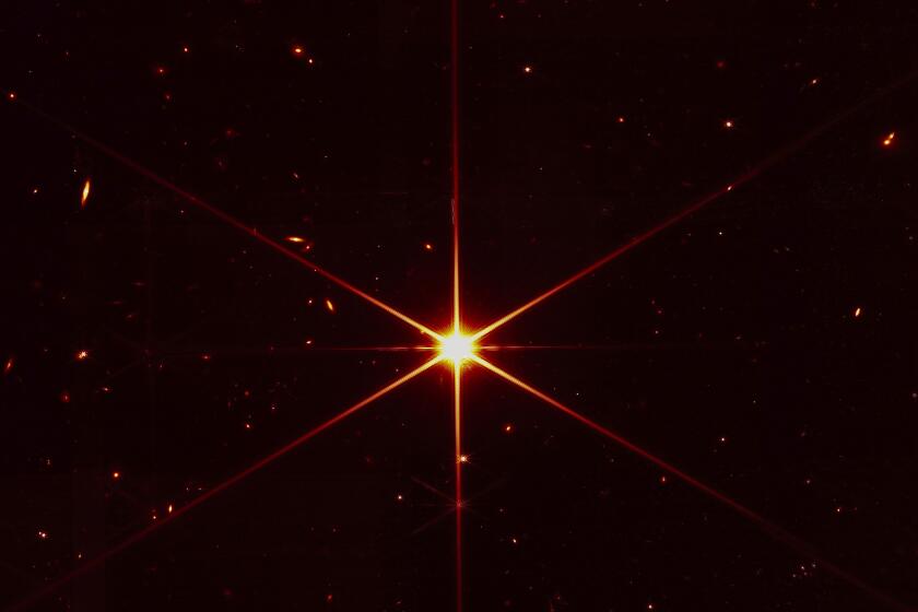 This image made available by NASA on Wednesday, March 16, 2022 shows star 2MASS J17554042+6551277 used to align the mirrors of the James Webb Space Telescope, with galaxies and stars surrounding it. The hexagonal shape of Webb’s mirrors and its filters made the shimmering star look more red and spiky. The first science images aren't expected until late June or early July. (NASA/STScI via AP)