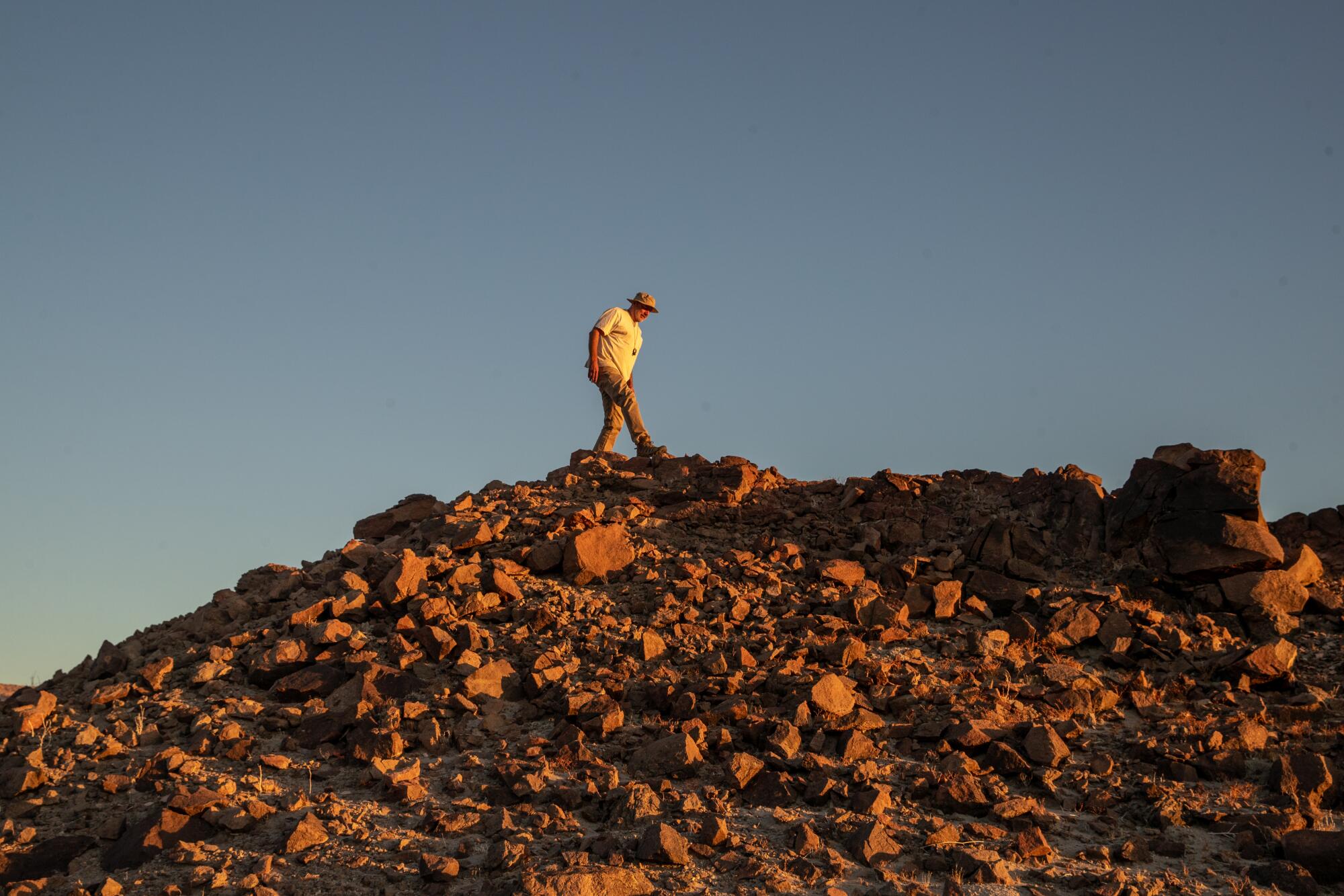 A lone figure walks atop a rocky hilltop.