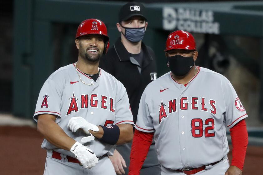 Albert Pujols stands by first base coach Jose Molina smiling.