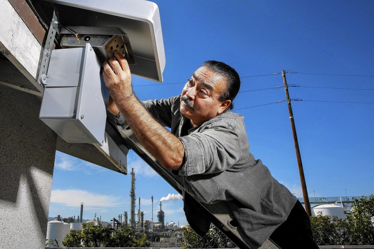 Jesse Marquez, executive director of Coalition for a Safe Environment, installs an air-quality device on the Peleti family's home in Wilmington near the Phillips 66 oil refinery.