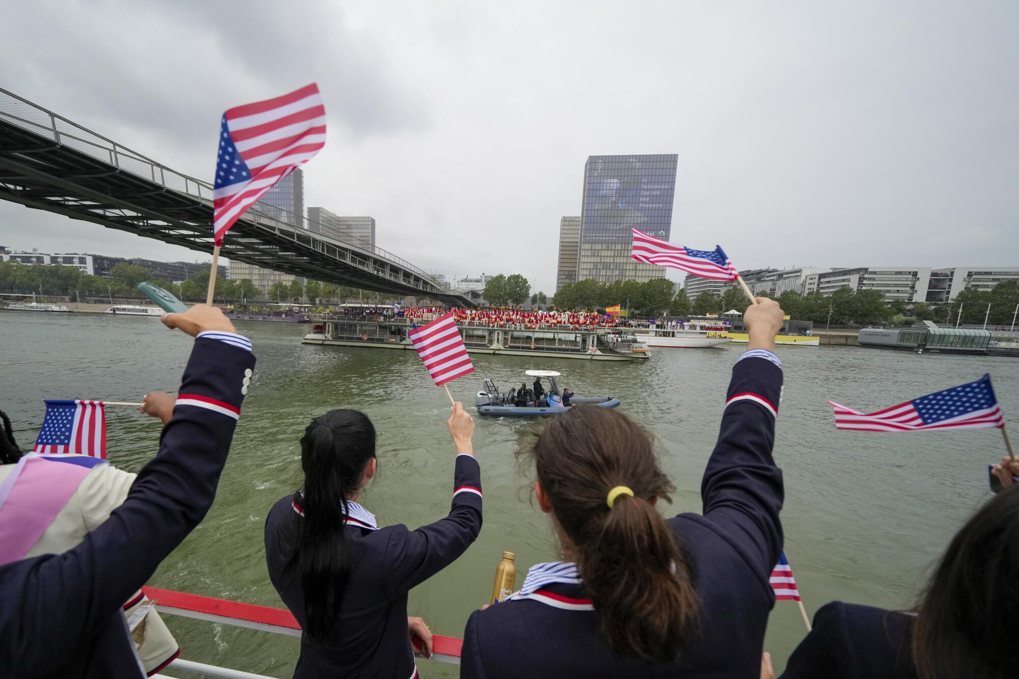Members of the United States Team wave flags as they travel along the Seine River in Paris.