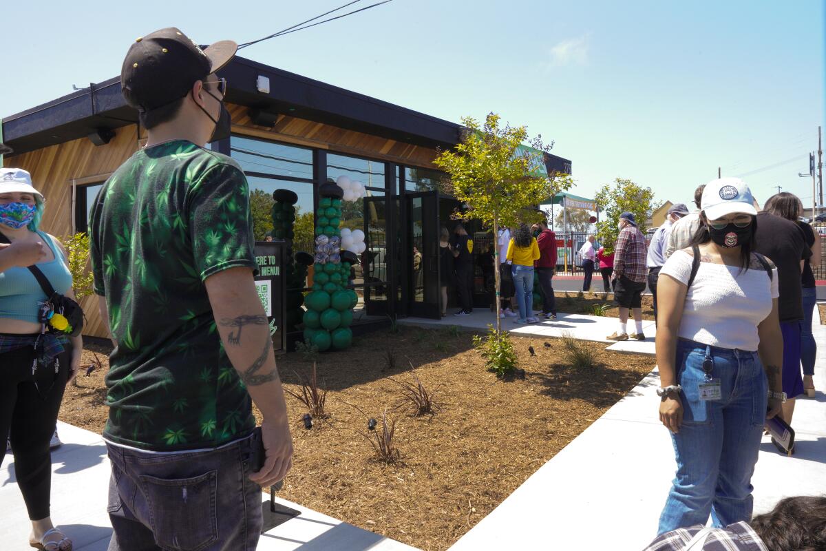 A line of people stand outside a cannabis dispensary.