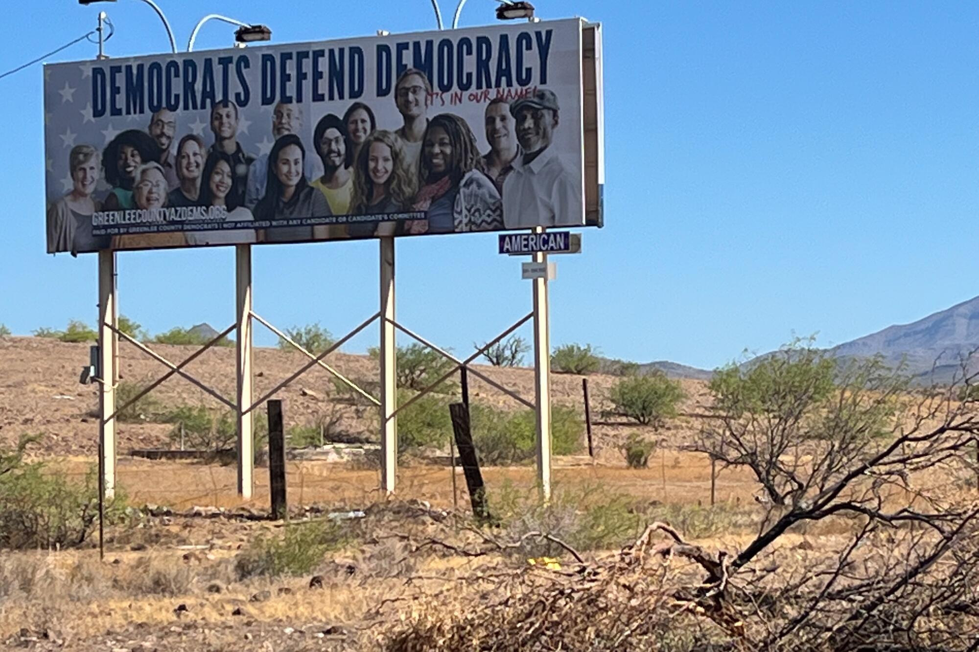 A billboard in a desert landscape dotted with shrubs depicts people under the words "Democrats Defend Democracy"