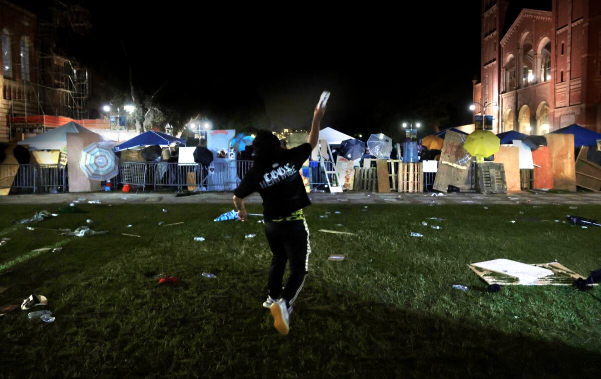 A person throws a bottle of water at an encampment at UCLA.