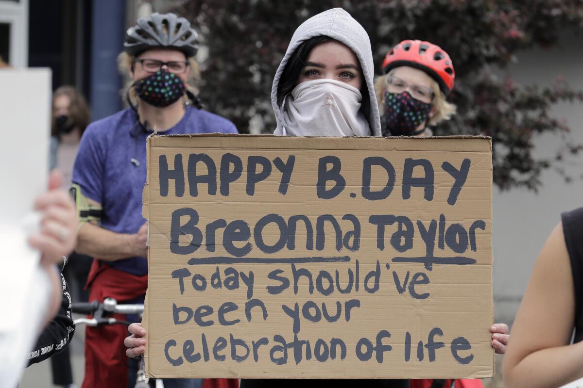 A protester holds a cardboard sign reading: "Happy B. Day Breonna Taylor — Today should've been your celebration of life."