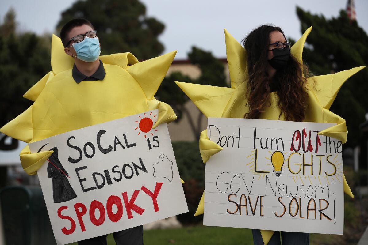 Two people in yellow spiky outfits symbolizing the sun hold signs, one of which reads, SoCal Edison is spooky 
