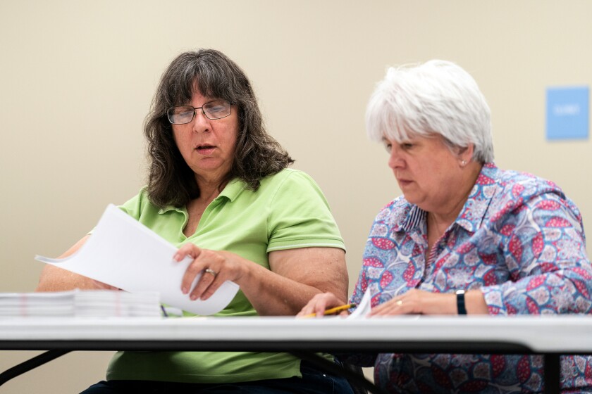 Two women sitting at a table look at ballots.
