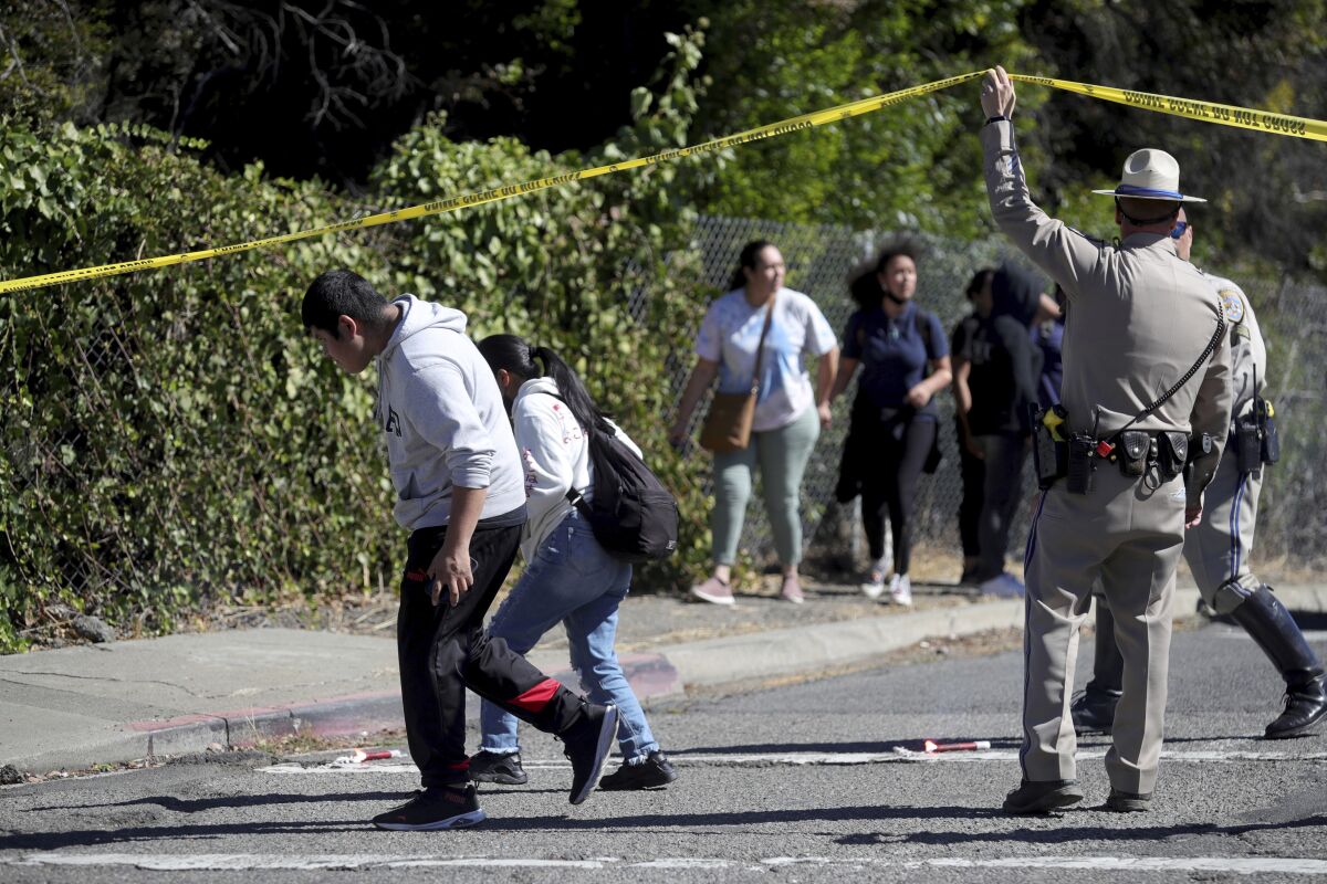 A California Highway Patrol officer lifts police tape to let parents and students leave a cordoned off area on Fountain Street following a shooting at a school campus in Oakland, Calif., on Wednesday, Sept. 28, 2022. (Ray Chavez/Bay Area News Group via AP)