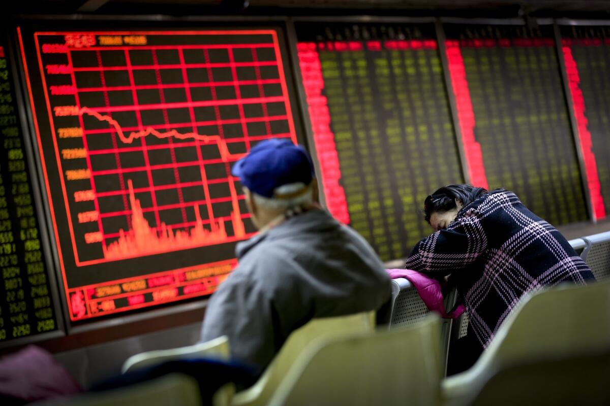 A woman takes a nap as a man looks at an electronic board displaying stock prices at a brokerage house in Beijing on Jan. 4.