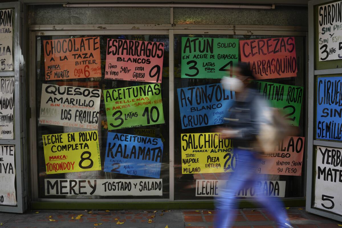 A person walks past a store with signs displaying grocery items and prices in Spanish.