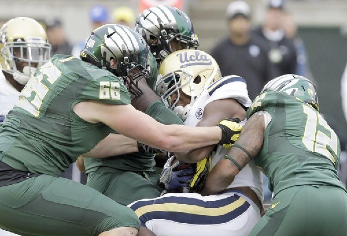 UCLA running back Paul Perkins is stopped by Oregon's Taylor Hart, left, and Brian Jackson, right, during the first half at Autzen Stadium.