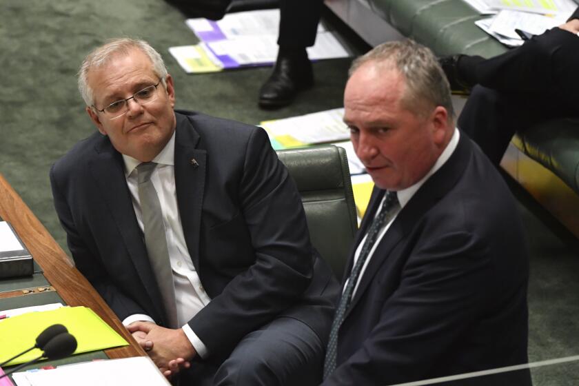 Australia's Prime Minister Scott Morrison, left, listens to Deputy Prime Minister Barnaby Joyce during question time in Parliament House in Canberra, Thursday, Oct. 21, 2021. Australia's Cabinet will on Monday, Oct. 25, 2021, consider conditions the government's junior coalition partner has placed on committing the national to a target of zero net carbon emissions by 2050. (Mick Tsikas/AAP Image via AP)