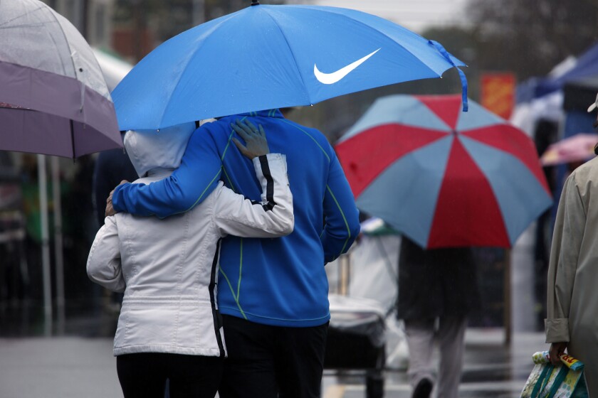 Darin and Terry Walters try to stay dry while shopping in the rain at the Mar Vista Farmers Market on Sunday.