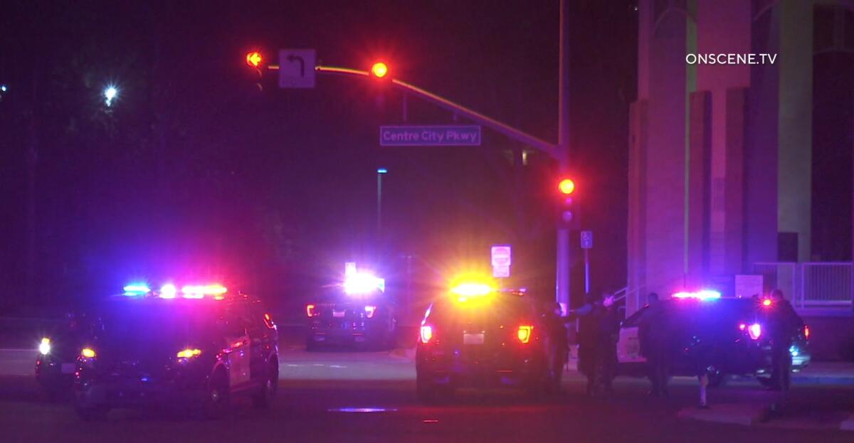 Several law enforcement vehicles with emergency lights on converge on an intersection in the dark.