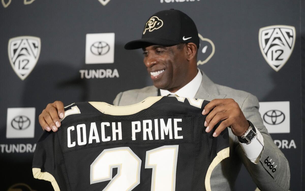 Deion Sanders holds up a No. 21 jersey with Coach Prime on it.