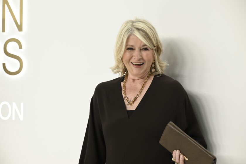 Martha Stewart smiles while wearing a black outfit and holding a black clutch purse.