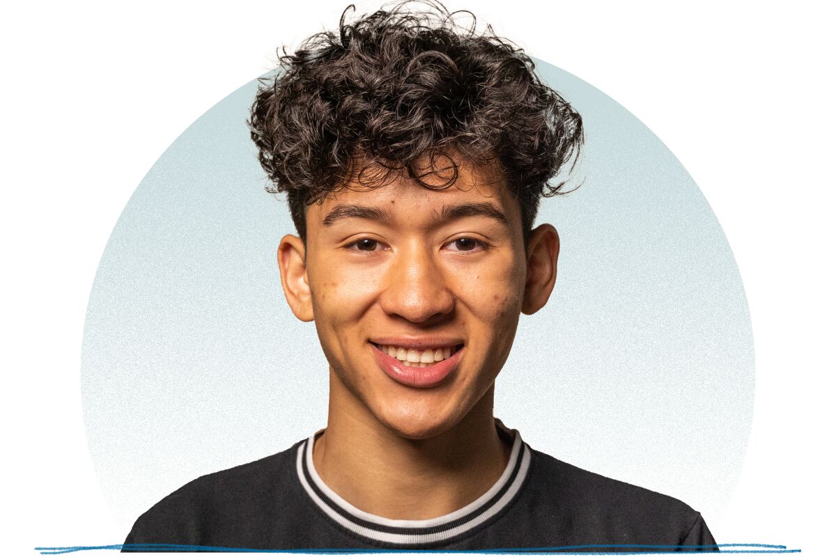 A young man with curly hair on top and a black shirt with black and white collar smiling for a portrait.