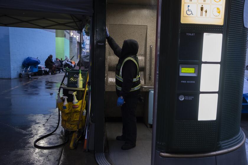 LOS ANGELES, CA - May 6: Urban Alchemy practitioner Robert Grasper, 60, cleans a toilet and keeps it safe in skid row during the night shift on May 6, 2021 in Los Angeles, CA. He said he was incarcerated for 30 years. Grasper greatly appreciates the opportunity to have a job he says. (Francine Orr / Los Angeles Times)