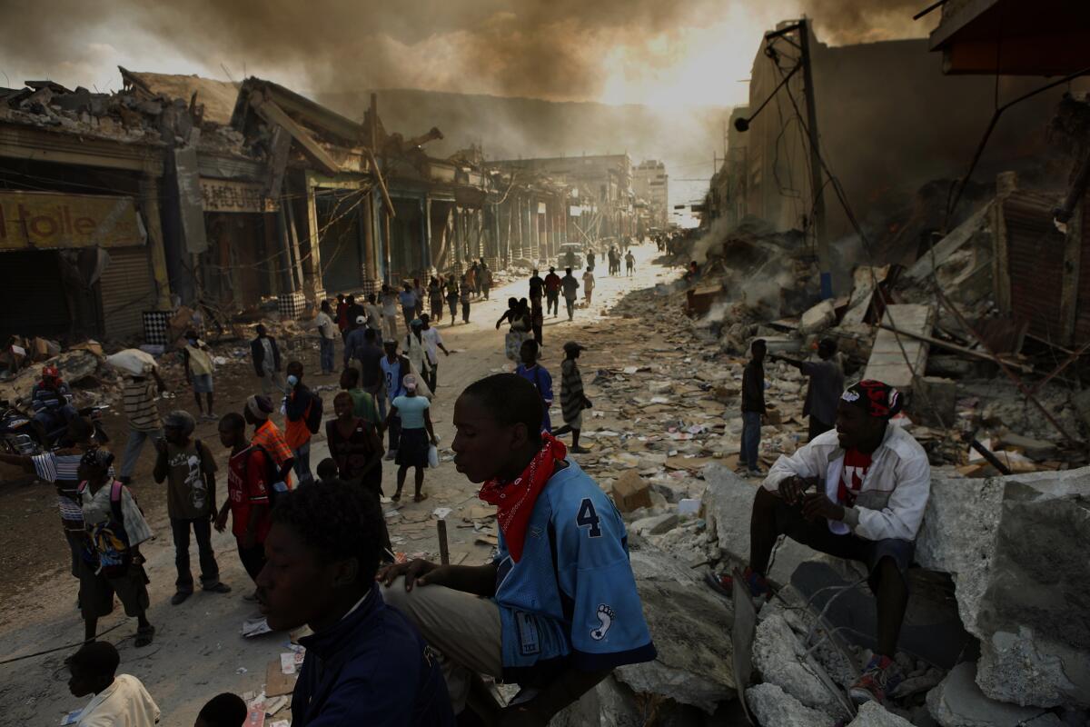 Smoke casts a pall as people walk amid rubble on a city street.