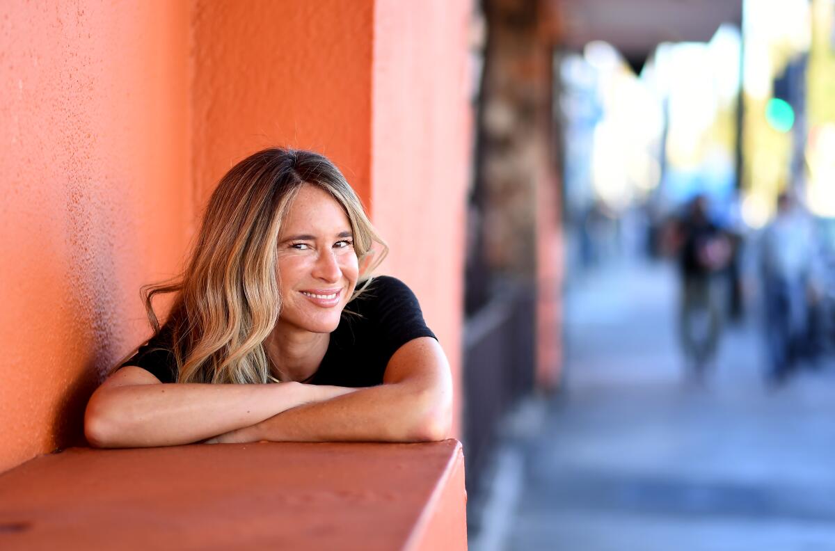 A smiling woman leans against an orange wall
