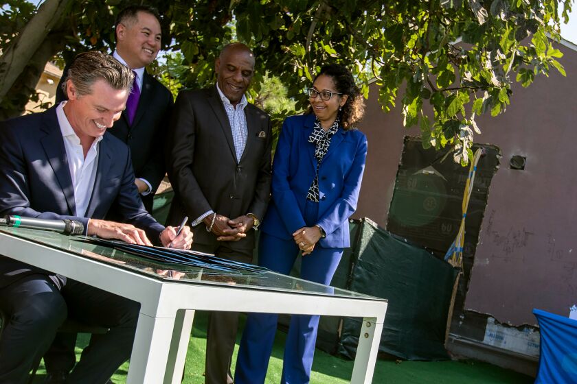 LOS ANGELES, CALIF. -- WEDNESDAY, OCTOBER 9, 2019: California governor Gavin Newsom, left, signs SB-330 Housing Crisis Act of 2019, in the backyard of homeowner Felicia Smith in Los Angeles, Calif., on Oct. 9, 2019. The governor signed several other housing bills in Smith’s backyard, where builders are converting her garage into a rental unit. (Brian van der Brug / Los Angeles Times)