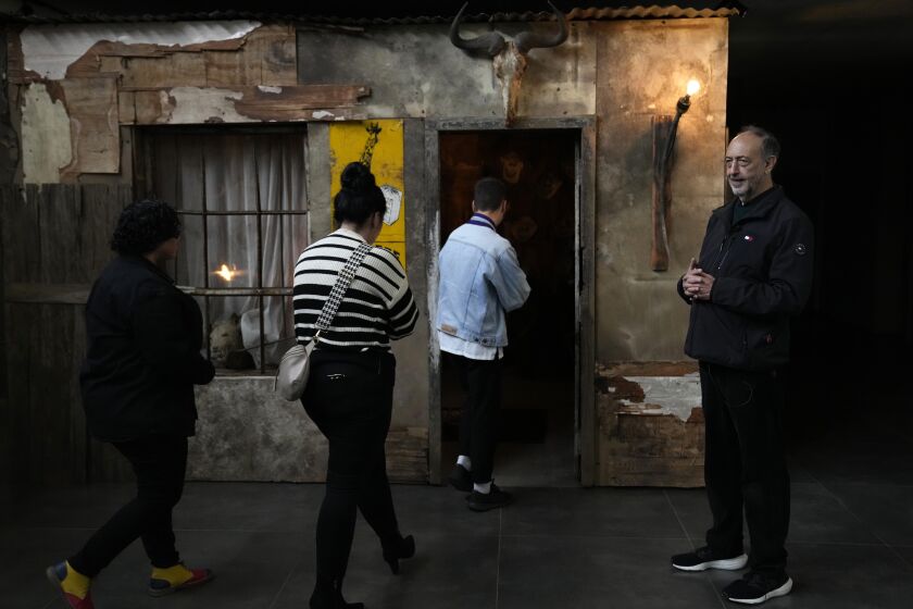 Artist and photographer Roger Ballen watches as visitors enter the "Shack" installation during an exhibition tour at Inside Out Centre for the Arts in Johannesburg, South Africa, Saturday, June 3, 2023. From the killing of elephants in the 18th century that began the ivory trade to the decimation of the rhino population from animal hunting, Ballen argues through his provocative art installations and multimedia artworks that humans remain at the forefront of the destruction of African wildlife. (AP Photo/Themba Hadebe)